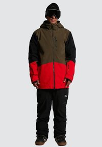 Veste de neige avec des blocs de couleurs vert olive, noir et rouge. Comprend une fermeture éclair sur le devant, une capuche ajustable et un pantalon de neige noir assorti.