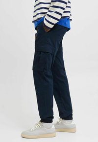 Marineblaue Cargo-Hosen mit Seitentaschen, elastischen Bündchen und lockerem Schnitt, kombiniert mit hellgrauen Sneakern und einem gestreiften Langarmshirt.