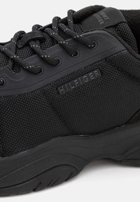 Sneaker nera con tessuto testurizzato, punta rinforzata e suola in gomma. Marchio "HILFIGER" sul lato con lacci rotondi e colletto imbottito.