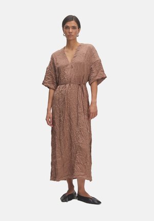 Braun, zerknittertes Kleid aus Stoff mit V-Ausschnitt, weiten Ärmeln und einem Bindegürtel. Die Länge reicht bis zu den Knöcheln und wird mit schwarzen, spitzen Schuhen kombiniert.