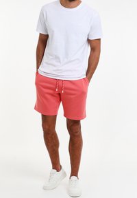 Camiseta blanca de algodón combinada con pantalones cortos coral. Los pantalones cortos tienen una cinturilla con cordón. Zapatillas blancas completan el conjunto.
