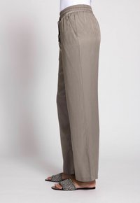 Leichte, beige Stoffhosen mit einem elastischen Bund, seitlichen Taschen und einem lockeren Schnitt, kombiniert mit flachen, gemusterten Slippern.