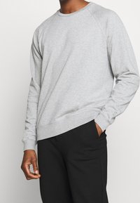 Sweat-shirt gris à col rond, poignets et ourlet côtelés. Fabriqué dans un tissu doux, avec des manches raglan et une coupe décontractée.