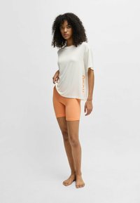 Light gray short-sleeve top with orange "Hugo" logo, paired with tight-fitting, mid-thigh orange shorts, showcasing a smooth texture.