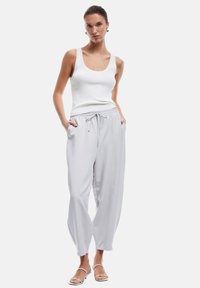Lichtgrijze taperende sweatpants met een elastische tailleband en trekkoord, gecombineerd met een aansluitend witte geribbelde tanktop en strapsandalen.
