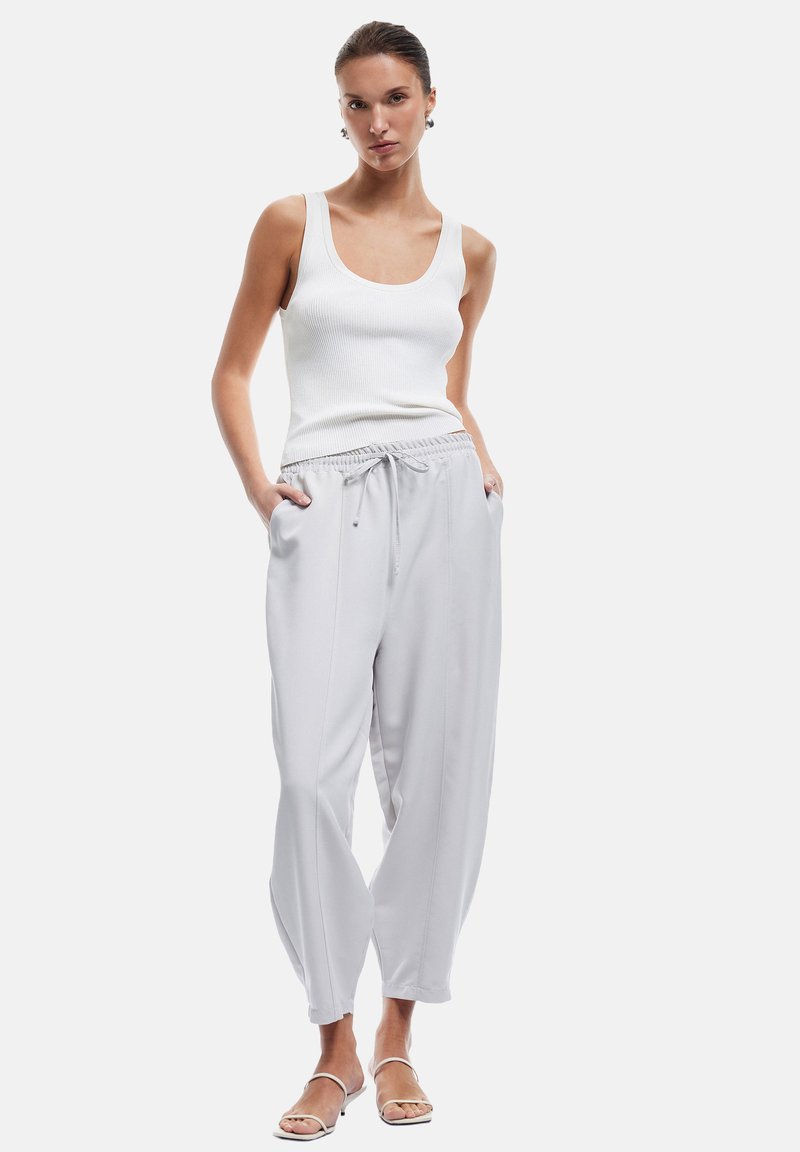 Lichtgrijze taperende sweatpants met een elastische tailleband en trekkoord, gecombineerd met een aansluitend witte geribbelde tanktop en strapsandalen.