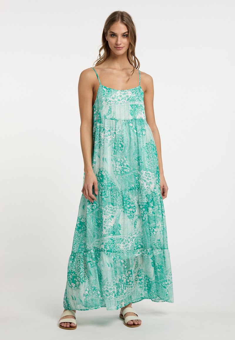 Rochie maxi în nuanțe de verde cu un model floral și paisley. Țesătură ușoară, bretele tip spaghetti și design în straturi. Sandale albe.