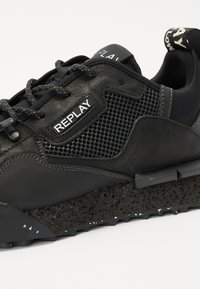 Schwarze Sneakers aus einer Mischung aus strukturiertem Leder und Mesh, mit einer klobigen, gesprenkelten Sohle und silbernen Hardware-Details.