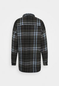 Camisa de franela negra y gris con un patrón de cuadros y acentos en azul claro, de manga larga y cuello clásico. Textura suave.