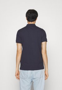 Marinblå kortärmad pikétröja i bomull, med en klassisk krage och rak nederkant, bärs med ljusblå denimjeans.