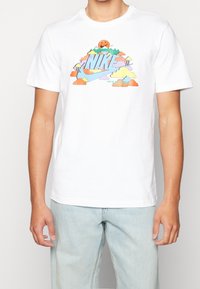 Camiseta de algodón blanca con un gráfico del logo de Nike multicolor, que incluye nubes y un sol, de manga corta y con cuello redondo.