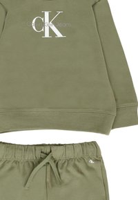 Olive green polarowy sweatshirt i dopasowane dresy. Sweatshirt ma okrągły dekolt i duże białe logo "CK". Dresy z elastycznym paskiem i sznurkiem.