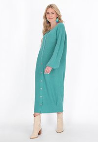 Abito lungo a maglia color turchese con maniche lunghe, scollatura a V e chiusura con bottoni frontale. Presenta un motivo testurizzato e bottoni dorati.