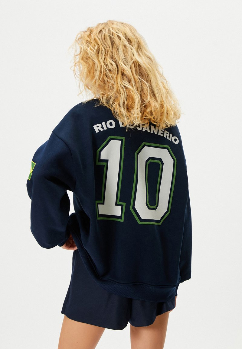 Marineblaue Sweatshirt mit grünen und weißen Akzenten, das auf der Rückseite "RIO DE JANEIRO" und die Nummer "10" deutlich zeigt.