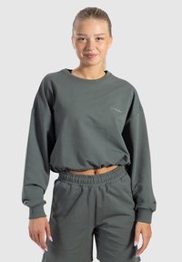 Felpa grigia corta con colletto rotondo, vestibilità ampia e bordo elastico in fondo, abbinata a pantaloni corti grigi coordinati. Presenta un branding discreto.