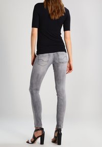 Vaqueros ajustados en denim gris claro, con una textura suave, diseño de cinco bolsillos y un ligero desgastado. Combinados con sandalias de tacón negro.