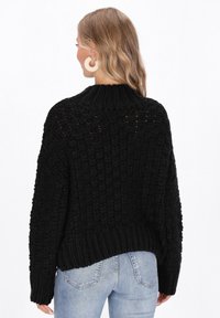 Fekete kötött pulóver texturált mintával, magas nyakkal és laza szabással. Bordázott szegély és ejtett vállak a nagyobb kényelem érdekében.