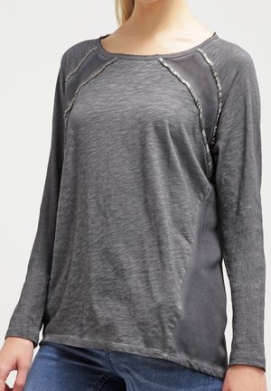 Chemise grise à manches longues avec un col rond, présentant un tissu texturé, des panneaux latéraux contrastants et de subtils accents de couture métallique.