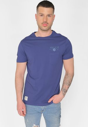 Blå kortærmet T-shirt lavet af bomuld, med en brystlomme og "TOP GUN" logo broderet i hvidt og blåt. Blød tekstur.