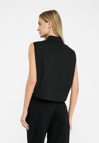 Top negru fără mâneci cu un design cu guler, evidențiind linii verticale strălucitoare și o textură netedă. Asortat cu pantaloni negri.