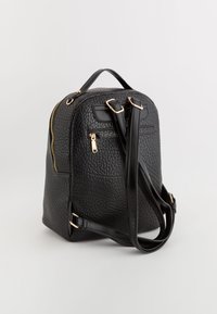Mochila de imitación de cuero negro con textura, cremalleras en tono dorado, correas ajustables y un asa en la parte superior. Incluye un bolsillo con cremallera en la parte frontal.