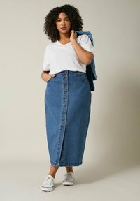 Jupe en denim bleu moyen à coupe droite, fermeture à boutons sur le devant, et deux poches latérales ; accompagnée d'un t-shirt blanc et de baskets blanches.
