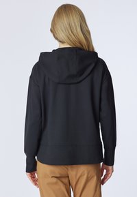 Felpa nera con cappuccio regolabile, polsini elasticizzati e vestibilità rilassata. Texture liscia, design semplice, senza motivi o hardware visibili.
