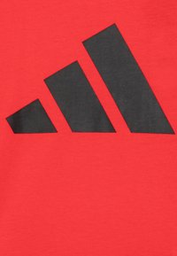 Röd bomulls t-shirt med en stor svart logotypdesign med tre ränder. Slät textur, standard crewneck-design.