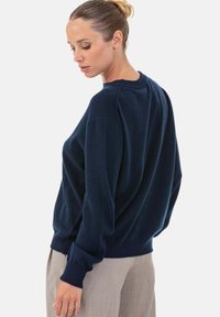 Pull en maille bleu marine avec une coupe décontractée, un col rond et des poignets côtelés. Texture douce, avec des épaules tombantes pour plus de confort.
