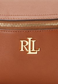 Brun skinnveske med en gullglidelås og et preget gulllogo "RL" tydelig vist på forsiden.