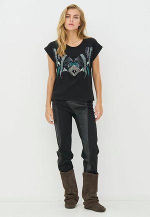 Sort kortærmet top med farverigt perlebesat design, kombineret med sorte bukser med teksturerede sidepaneler og brune ruskindsstøvler.