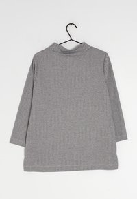 Šedý top s dlouhým rukávem z texturované látky s rybí kostí, s vysokým límcem a bočními rozparky na lemu. Visí na čern ém háčku.