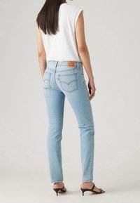 Ljusblå denimjeans med slim fit, hög midja, standardfickor och en läderlapp på baksidan av midjan. Slät textur.