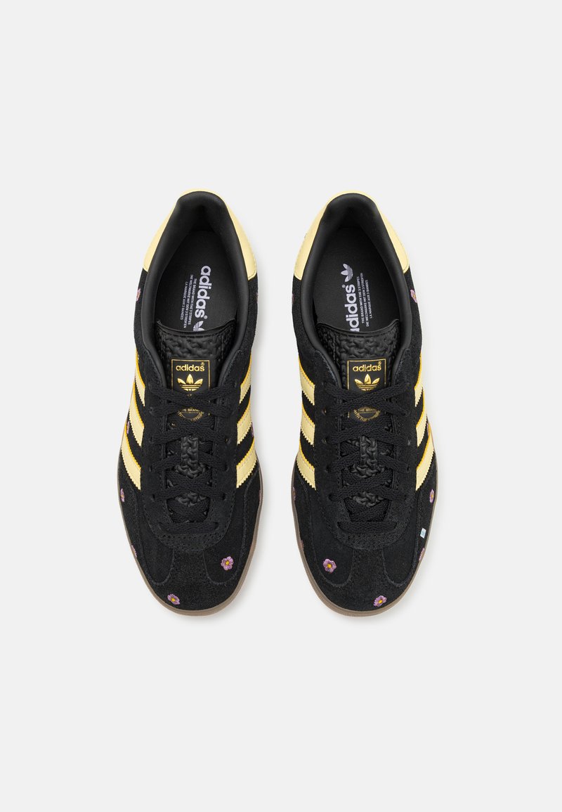 Sneakers in suede neri con strisce gialle e accenti floreali. Presentano una superficie testurizzata, punta arrotondata e chiusura con lacci.