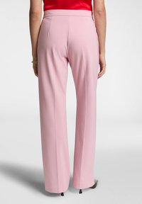 Pantaloni rosa a vita alta realizzati in tessuto liscio, con taglio dritto e dettagli minimi, dotati di cuciture sartoriali e senza tasche.