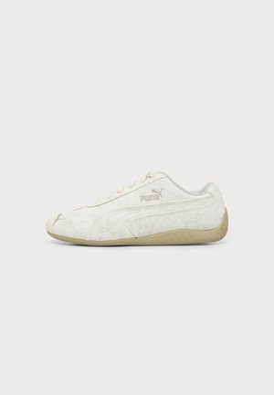 Adidași Puma albi cu talpă bej, vedere laterală, afișând logo-ul Puma și un design minimalist pe un fundal simplu și deschis.
