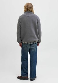 Grijze fleece jas met een hoge kraag, gedragen over een geruit shirt. Gecombineerd met blauwe denim jeans en stevige bruine laarzen.
