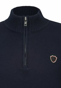 Marineblauer Strickpullover mit hohem Kragen, halbseitigem Reißverschluss und einem kleinen Wappen-Logo mit rot-, weiß- und grünen Akzenten auf der Brust.