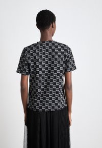 Μαύρο μπλουζάκι με σχέδιο που καλύπτει όλη την επιφάνεια και απεικονίζει αλληλένδετα λογότυπα NY. Έχει κοντά μανίκια και στρογγυλή λαιμόκοψη, κατασκευασμένο από απαλό ύφασμα.