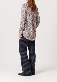 Chemise à manches longues en tissu léger avec un motif floral aux couleurs pastel. Associée à un pantalon ample à larges rayures bleu marine.
