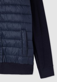 Giacca blu navy con pannello frontale in nylon trapuntato, maniche in maglia, polsini a costine e una tasca a filetto orizzontale sulla parte frontale.