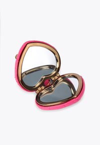 Specchio compatto a forma di cuore con un esterno rosa testurizzato e rifinitura metallica dorata. Si apre per rivelare due superfici riflettenti.