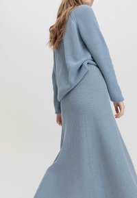 Hellblauer Strickpullover und passender Rock mit gerippter Textur. Der Pullover hat eine leicht übergroße Passform; der Rock fällt bis zum Boden.