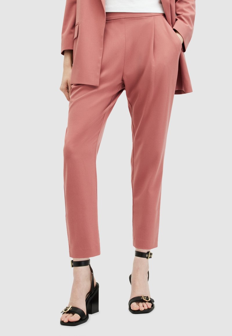 Personne portant un pantalon rose taillé sur mesure et un blazer assorti, associé à des sandales noires à talons hauts avec des brides à la cheville.