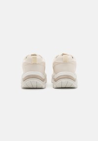 Beige sneakers with a smooth leather upper and a thick white rubber sole. Featuring a pull tab at the heel and subtle tonal accents.