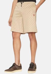 Pantalones cortos beige con un patrón sutil, que cuentan con una cintura ajustable con cordón, bolsillos laterales y un pequeño acento rojo cerca del dobladillo. Ajuste casual, de largo hasta la rodilla.