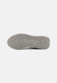 Gray rubber shoe sole featuring a triangular tread pattern and raised branding. Designed for traction with a textured surface.