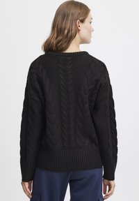 Svart stickad tröja med kabelmönster, ribbad fåll och muddar. Bakvyn visar textur och design utan ytterligare detaljer.