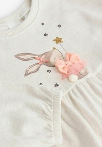 Light cream fabric dress featuring a rabbit appliqué with pink accents, decorative stars, and textured frills along the skirt.
