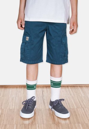Blå cargo shorts med to sidelommer, parret med hvide ankelstrømper med grønne striber, og grå sneakers med hvide såler.